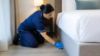 Cleaner cleaning the floor edge beside a guest room bed